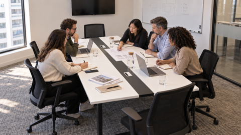 Colleagues discussing documents and laptops around a Lurpes conference table in an office meeting